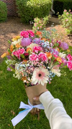 a bouquet of flowers is being held by a person's hand in the grass