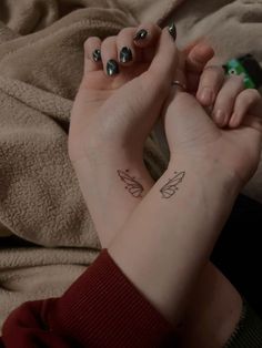 two hands holding each other with small tattoos on their wrists and fingers, one has a butterfly tattoo on its left wrist