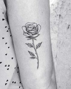 a black and white photo of a single rose tattoo on the left arm, with hearts in the background