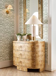 a dresser with a lamp on top of it next to a wallpapered wall