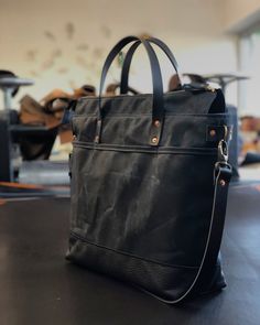 Tote bag with luggage handle attachment in American heavy weight waxed canvas. The color is black for the body and black leather bottom. I made it into an everyday bag perfect for the office, with leather handles, shoulder strap, and 3 outside pockets Closing with a zipper on top. And on the backside a luggage handle attachment Including a leather shoulder strap, adjustable and detachable. Fully lined with a cotton canvas and double inside pockets. All the bags are made and designed by myself an Luxury Coated Canvas Bag With Gunmetal Hardware, Waxed Canvas Satchel Briefcase For Everyday, Everyday Waxed Canvas Satchel Briefcase, Everyday Waxed Canvas Briefcase With Leather Trim, Black Canvas Bag With Leather Trim, Black Canvas Bag With Leather Trim For Everyday, Black Canvas Weekender Bag With Leather Handles, On-the-go Black Leather Canvas Bag, Black Leather Canvas Bag For On-the-go