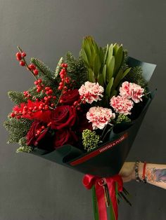 a person holding a bouquet of flowers with red and green foliage in the center, on a gray background