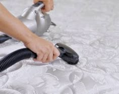 a person using a vacuum to clean a bed