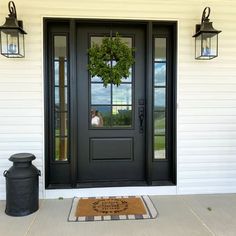 a black front door with a wreath on it and two lanterns hanging from the side