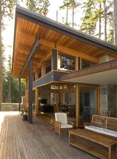 a wooden deck with two chairs and a bench next to a house in the woods