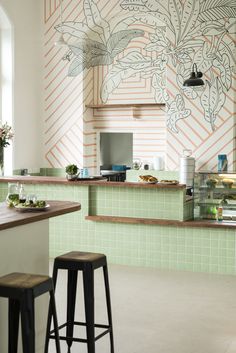 a green tiled kitchen with stools in front of the counter and an art work on the wall