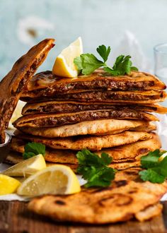 a stack of pancakes with lemon wedges and parsley