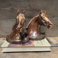 two bronzed horses head on top of each other with books in front of them