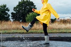 Stock Image: Woman having fun on the street after the rain. Cropped woman wearing rain rubber boots and yellow raincoat walking into puddle with water splash and drops. Fall weather. Selective focus Yellow Rain Boots Outfit, Woman Having Fun, Rain Boot Outfit, Yellow Rain Boots, Water Splash, Yellow Raincoat, Character References, After The Rain, Fun Size