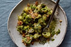 a white plate topped with broccoli covered in pesto and walnuts next to a fork