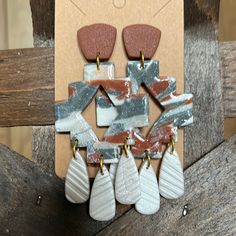 a pair of earrings with different shapes and colors on them sitting on top of a piece of wood