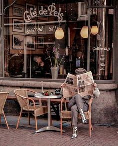 a person sitting at a table with a newspaper in front of a storefront window