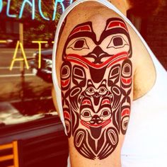 a man with a tattoo on his arm in front of a storefront window, wearing a white tank top