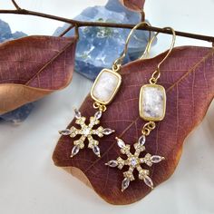 These beautiful earrings feature shimmering white moonstone, known for its ethereal glow and captivating play of light, paired with delicate snowflake accents. The dangle design adds movement and a touch of charm, making them perfect for any occasion.  Lightweight and comfortable, these earrings are ideal for both everyday wear and special events. Their unique combination of natural stones and intricate detailing makes them a standout piece that enhances your style. Natural moonstone, 14K gold plated brass. Take off your jewelry while working out, cleaning, gardening, showering, bathing or swimming in chlorinated or salt water. Ethereal Jewelry, Forever Jewelry, White Moonstone, Charm Making, Jewelry Ring Box, Men's Jewelry Rings, Watch Necklace, Womens Jewelry Rings, Inspirational Gifts