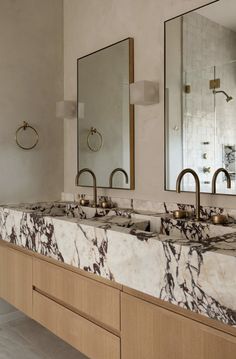 a bathroom with marble counter tops and two mirrors on the wall, along with gold faucets