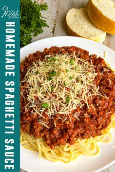 a white plate topped with spaghetti and meat sauce next to bread on a wooden table