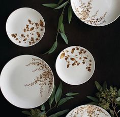 four white plates with gold leaf designs on them and some green leaves in the middle