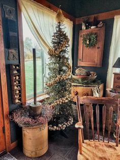 a small christmas tree in the corner of a room with two chairs and a window