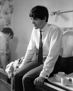 black and white photograph of a man sitting on a counter with coffee cups in front of him