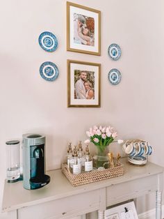 a white table topped with pictures and vases filled with flowers next to a coffee maker