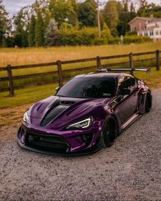 a purple sports car parked in front of a wooden fence on the side of a road