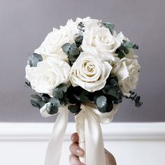 a bridal bouquet with white roses and greenery is held by a woman's hand