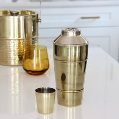 three metal cups sitting on top of a white counter next to each other and one gold cup in the middle