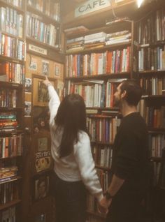 two people standing in front of a bookshelf with many books on the shelves