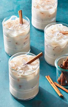 four glasses filled with drinks on top of a blue table next to cinnamon sticks and anisette