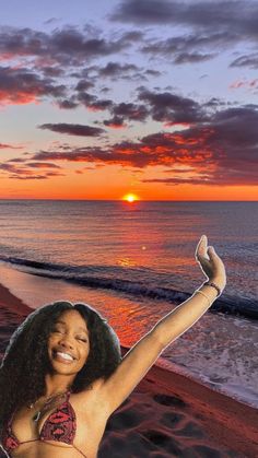 a woman standing on top of a beach next to the ocean with her arms in the air