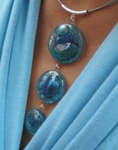 a close up of a woman wearing a blue shirt and necklace with three glass beads on it