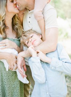 a man and woman holding a small boy in their arms while he kisses the baby's forehead