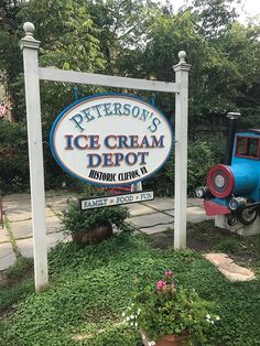 a sign for the ice cream depot in front of some bushes and trees with flowers