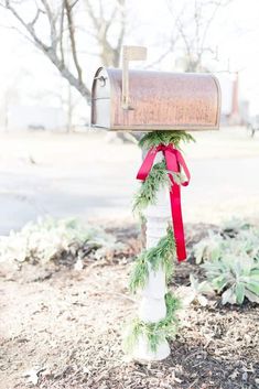 a mailbox with a red ribbon tied around it's post and some greenery