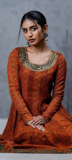 a woman sitting on the ground wearing an orange dress