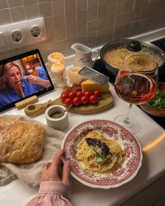 a person sitting at a kitchen counter with food and wine in front of the computer