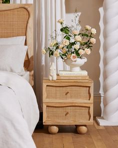 a white vase filled with flowers sitting on top of a wooden dresser next to a bed