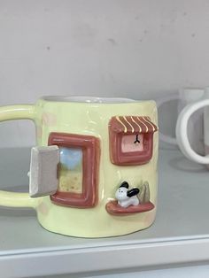 two coffee mugs sitting next to each other on a shelf with one holding a cat