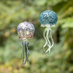 two glass jellyfish ornaments hanging from strings in front of green trees and foliages