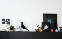 there is a black bird sitting on the shelf next to some potted plants and pictures