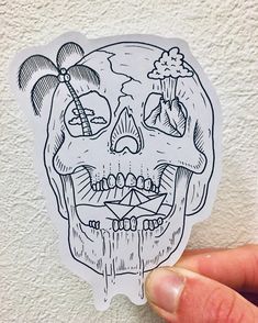 a hand holding up a sticker with a drawing of a skull and palm trees on it