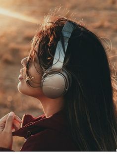 a woman with headphones on looking at the sun through her earbud's