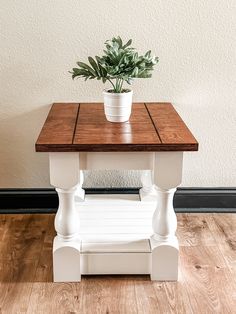 a small wooden table with a potted plant on top and wood flooring in the background