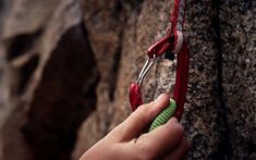 a person is holding some scissors in their hand while climbing up a rock face wall