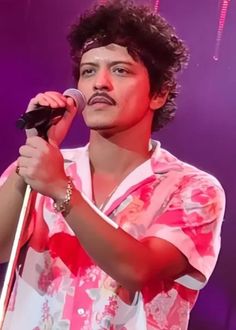 a man holding a microphone in his right hand and wearing a pink shirt on stage