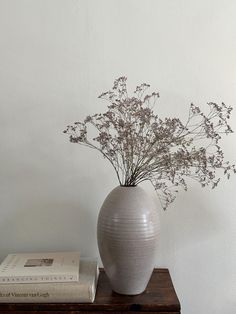 a white vase with some flowers in it on a table next to a stack of books