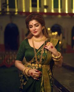 a woman in a green and gold sari is holding her hand on her shoulder