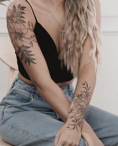 a woman sitting on the floor with her arms crossed and flowers tattooed on her arm