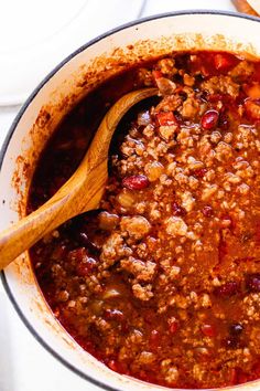 a pot filled with chili and meat on top of a stove next to a wooden spoon