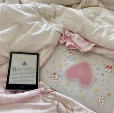 an electronic device sitting on top of a bed covered in pink sheets and white sheets